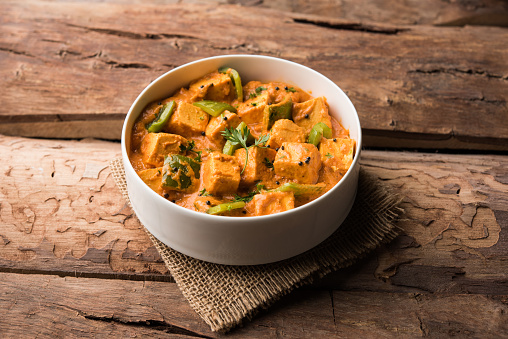 Malai or achari Paneer in a gravy made using red gravy and green capsicum. served in a bowl. selective focus